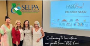 ID: Four women standing together in a conference hall. Above their heads on the wall behind them is the SELPA logo and the words SELPA Administrators of California, Special Education Local Plan Area. On the right side of the photo is a screen with the title powerpoint slide showing the FASDNow! logo and the words Ed Code 56332. Many of the logos of the members of the FASD Now! Alliance are at the bottom of the screen. At the bottom right of the photo in a font that mimics handwriting is written 